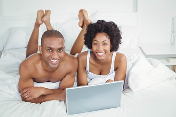 Fototapeta premium Smiling couple using laptop on bed