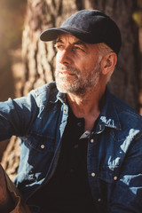 Mature man wearing cap sitting by a tree
