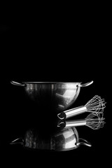 Stainless steel bowl with metal whisker aside on black background from side with reflection vertical composition