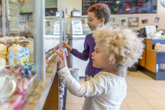 Mixed race girls picking cupcakes in bakery
