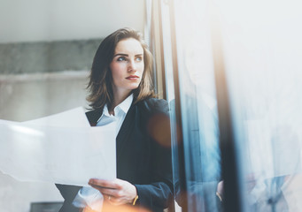 Portrait businesswoman wearing suit, talking smartphone and holding papers in hands. Open space...