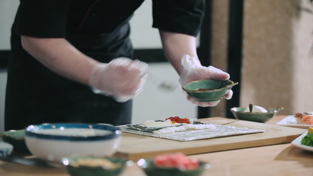 Sushi master adds caviar in to roll