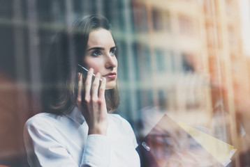 Picture businesswoman wearing modern suit, talking smartphone and holding papers in hands. Open space loft office. Panoramic windows background. Horizontal mockup. Film effect