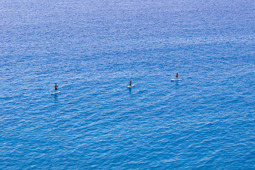 Three paddleboarders surrounded by blue sea