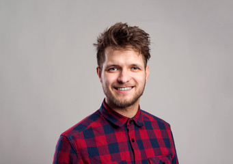 Hipster man in checked shirt smiling, against gray background.