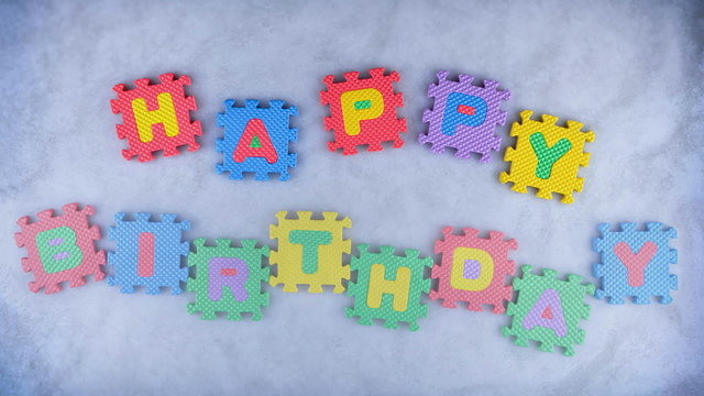 Words Happy Birthday made of alphabet puzzles appearing word by word on the blue texture for background. Different color letters.