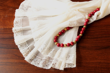 A white lace petticoat with a red coral necklace with golden spheres on a brown, wooden table. - obrazy, fototapety, plakaty