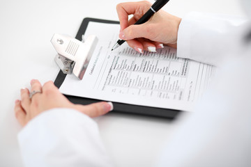 Close-up of a female doctor filling  out application form , sitting at the table in the hospital