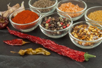 Various kinds of spices in glass bowls on a slate background. Preparation for cooking spicy food. Spices for master cook. The spice trade. Sale of spices in the kitchen.
