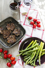 Grilled lamb with green asparagus, grill pan, red vine, wood background.