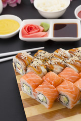 Sushi roll on a wooden plate ( gete ) with sauces ginger and wasabi over black background