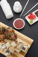 Tempura and shavings of tuna sushi roll on wooden plate ( gete ) with ginger wasabi chopsticks and sauces over black background