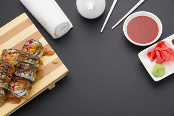 Tempura sushi roll on wooden plate ( gete ) with ginger wasabi chopsticks and sauces over black background