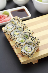 shrimp sushi roll on wooden plate ( gete ) with ginger wasabi and sauces over black background