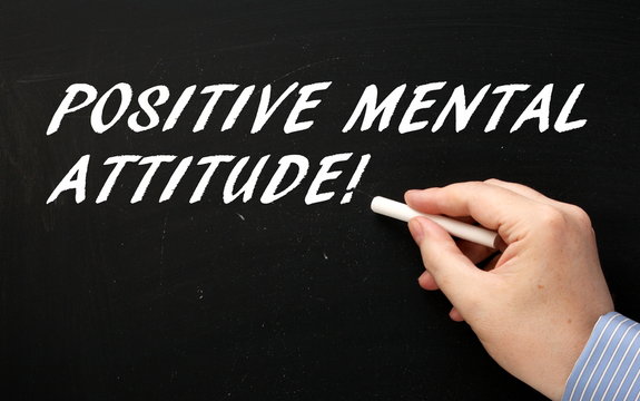 Hand writing the words Positive Mental Attitude in white text on a blackboard as a reminder of one of the attributes to look for in people