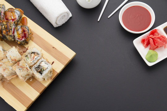 Sushi roll on a wooden plate ( gete ) with sauces ginger and wasabi over black background