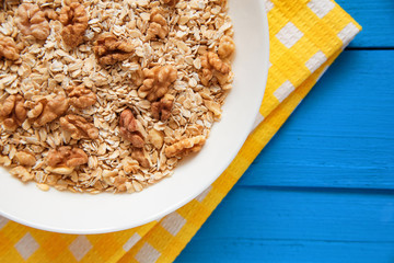 Dry oatmeal flakes  with walnuts in a white plate on a blue wood