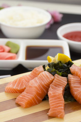 Japanese cuisine. Salmon sashimi on a wooden plate with ginger wasabi and sauces over black background