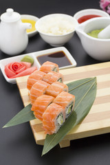Japanese cuisine. Salmon sushi on a wooden plate with ginger wasabi and sauces over black background