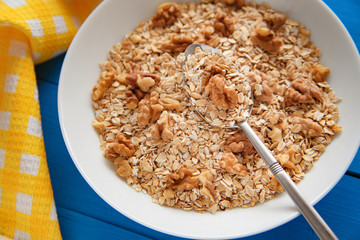 Dry oatmeal flakes  with walnuts in a white plate on a blue wood