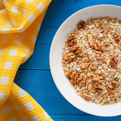 Dry oatmeal flakes  with walnuts in a white plate on a blue wood