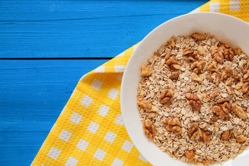 Dry oatmeal flakes  with walnuts in a white plate on a blue wood