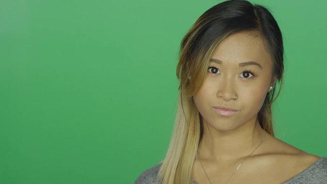 Cute Asian girl glaring, on a green screen studio background