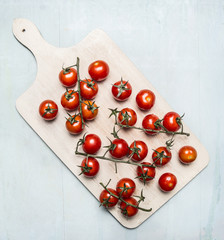 Naklejka na ściany i meble Fresh cherry tomatoes on a branch on a white cutting board on wooden rustic background top view