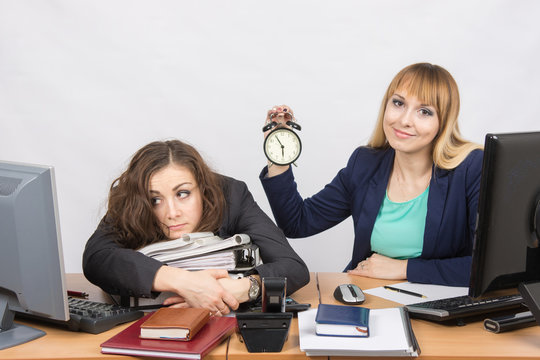 Two girls in the office at the end of the day, one positive, the other exhausted