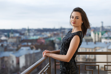 Attractive young beautiful girl wearing classical black dress posing on the balcony of luxury building.