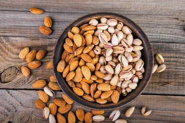 Top view of almonds and pistachios on a wooden bowl, rustic background.