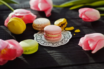 Obraz na płótnie Canvas A beautiful flowers pink tulips with colorful macaroons laid on dark wooden background with Lacy napkin