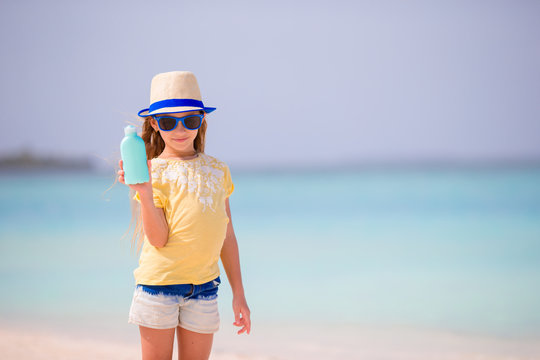 Little Adorable Girl With Suntan Lotion Bottle On The Beach