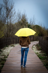 Une personne sous son parapluie jaune sur un chemin de plage en bois 