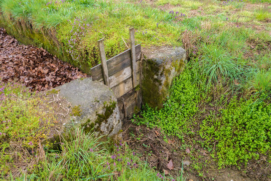 Chiusa in cemento  con saracinesca in legno in un fossato per regolare il corso dei flussi  d’acqua  per l’irrigazione