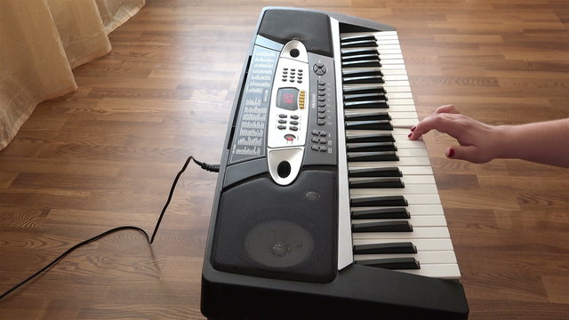 beautiful female hand with red nails composes music on the keyboard by pressing the white keys