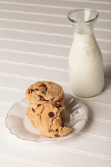 Freshly baked homemade chocolate chip cookies stacked up with a vintage milk bottle on a corrugated white background
