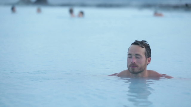 Geothermal spa. Man relaxing in hot spring pool on Iceland. Young man enjoying bathing relaxed in a blue water lagoon Icelandic tourist attraction.