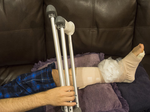 Man With a Sprained Ankle on Couch Holding Crutches