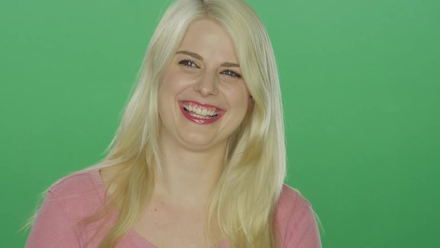 Beautiful blonde woman laughs and throws her hair back and starts dancing, on a green screen studio background