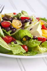 Close up shot of fresh homemade southwest black bean lime salad with corn, cherry tomatoes, lettuce, avocado, and black beans with vinaigrette dressing for clean eating