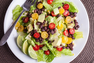 Homemade southwest black bean lime salad with corn, cherry tomatoes, lettuce, avocado, and black beans with vinaigrette dressing for clean eating - close up
