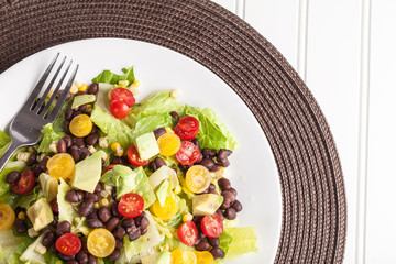 Top view of homemade southwest black bean lime salad with corn, cherry tomatoes, lettuce, avocado, and black beans with vinaigrette dressing for clean eating