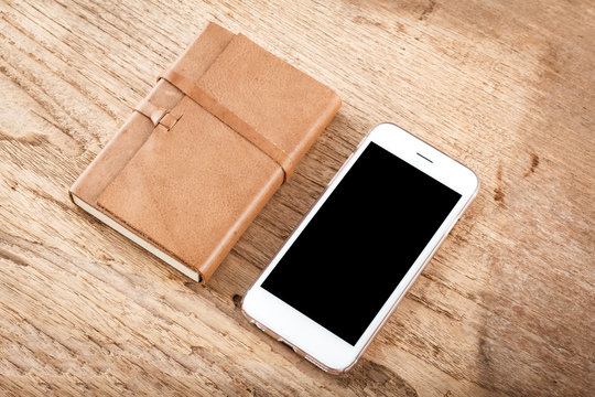 Brown leather notebook and Mobile phone on wood table background