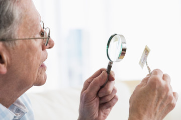 Senior Caucasian man examining stamp with magnifying glass