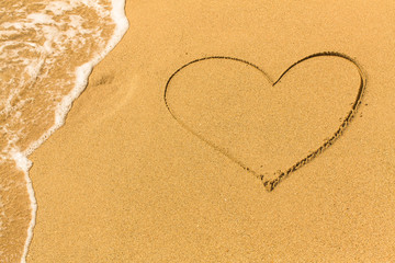 Fototapeta na wymiar Heart drawn on the sand of a beach with the soft wave.
