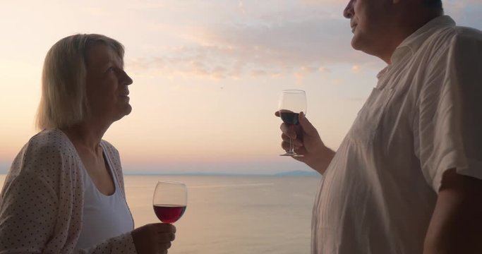 Senior man and woman drinking wine and enjoying picturesque view to the sea and evening sky. Tender relations