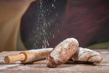 two loafs of bread with a rolling pin and flour being sprinkled on it
