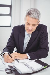 Businessman writing in spiral notebook in office