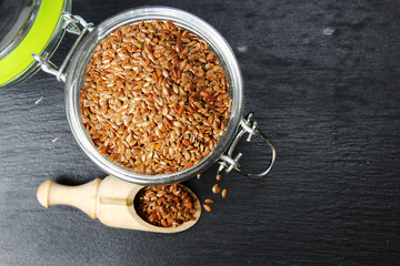 Flax seeds in a jar on a grey background with copy space, selective focus.